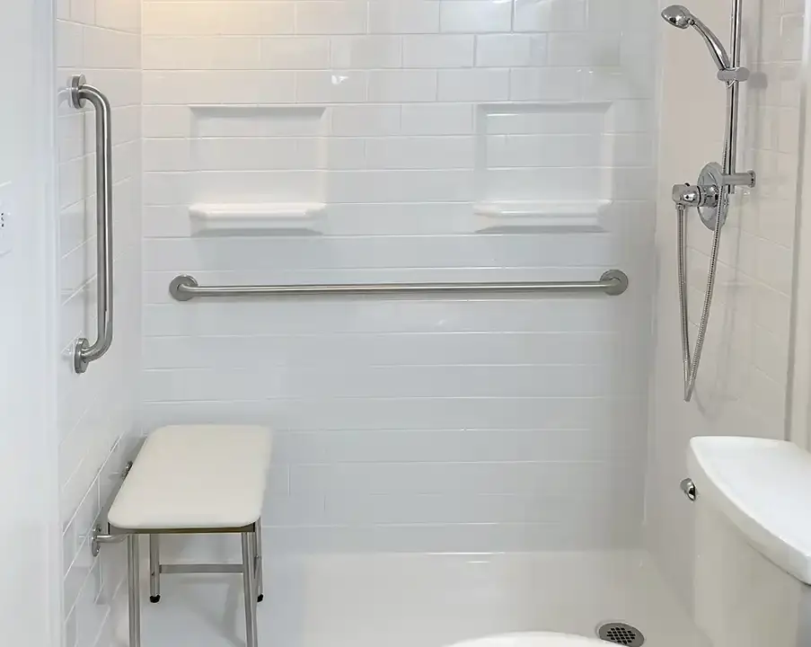 A modern, accessible shower stall with grab bars and a handheld showerhead, designed for ease of use by individuals with mobility challenges. The spacious stall features a barrier-free entry, ensuring safe and convenient access.