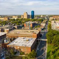 A scenic view of downtown Lexington, Kentucky, featuring historic buildings, lush greenery, and a backdrop of the city skyline under a bright blue sky.